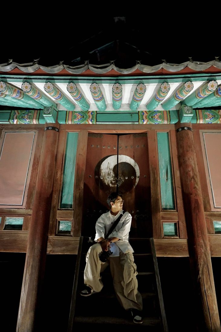 밤 한옥 문 앞에 카메라를 들고 앉은 작가